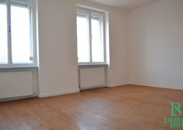 Heller Raum mit Holzdielenboden, weißen Wänden und zwei großen Fenstern.