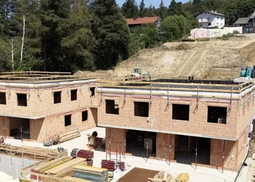 Baustelle mit mehreren im Bau befindlichen Reihenhäusern in hügeliger Landschaft.