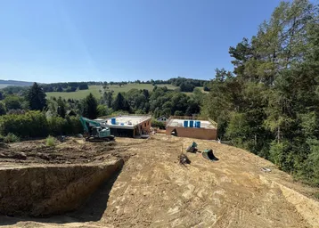 Weitläufige Baustelle mit Erdarbeiten und Blick auf die grüne Hügellandschaft.