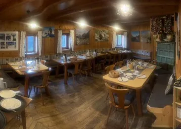 Geräumiger Speisesaal einer Berghütte mit Holzwänden, Holzböden und mehreren Tischen für Gäste.