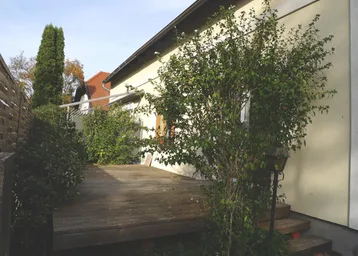 Geräumige Holzterrasse am Haus, umgeben von grünen Büschen, ideal für entspannte Stunden im Freien.