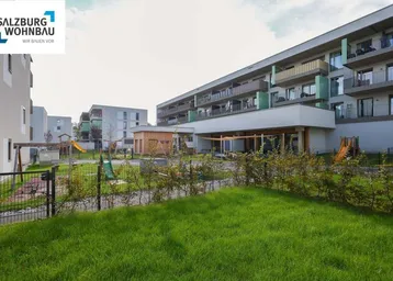 Moderner Wohnkomplex mit ansprechenden Balkonen, umgeben von Grünflächen und einem Kinderspielplatz.