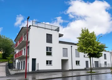 Modernes Mehrfamilienhaus mit weißer Fassade, Balkonen und Flachdach unter blauem Himmel.