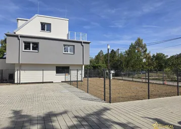 Modernes Gebäude mit grauer Fassade, gepflastertem Parkplatz und eingezäuntem Grundstück.