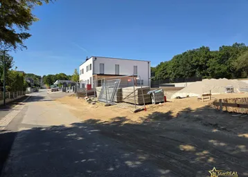 Baustelle mit einem modernen Neubau im Hintergrund und vorbereitetem Gelände.