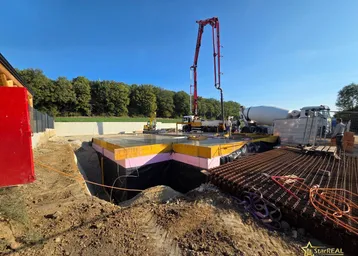 Eine Betonpumpe gießt das Fundament für ein neues Gebäude auf einer ländlichen Baustelle unter blauem Himmel.