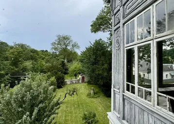 Blick aus einem historischen Fenster auf den weitläufigen Garten und die umliegende grüne Landschaft.