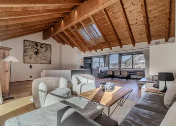 Helles Wohnzimmer mit Holzbalkendecke, Kamin und Panoramablick auf die Berge.