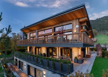 Moderne Holzfassade eines Chalets mit mehreren Balkonen und Bergblick bei Sonnenuntergang.