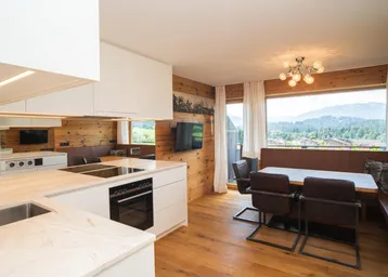 Moderne offene Küche mit Essbereich, Holzwänden und Bergblick durch große Fenster.