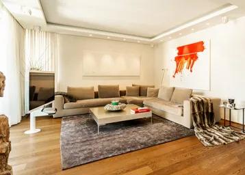 Helles Wohnzimmer mit großem Ecksofa, Holzboden und moderner Kunst an den Wänden.