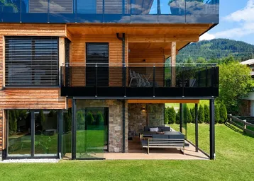 Moderne Holzfassade mit Glasbalkonen und einer möblierten Terrasse im Erdgeschoss mit Bergblick.