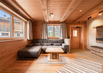 Gemütliches Wohnzimmer im alpinen Stil mit Holzwänden, geschnitzter Holzdecke und bequemer Eckcouch.