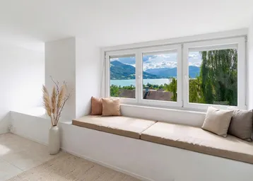 Heller Wohnbereich mit integrierter Sitzbank am Fenster und atemberaubendem Blick auf den See und die Berge.