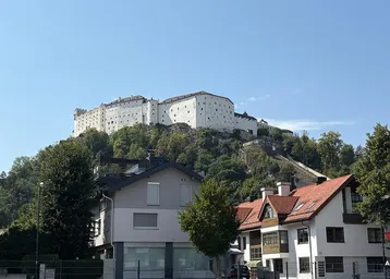 Blick auf eine historische Festung auf einem Hügel mit Wohnhäusern im Vordergrund unter blauem Himmel.