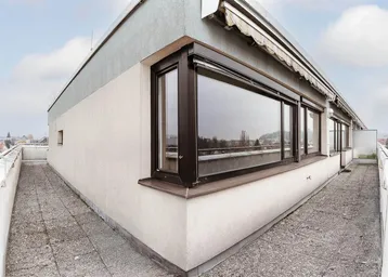Geräumige Dachterrasse mit Betonplattenboden, großen Fenstern und Markise, ideal für entspannte Stunden mit Fernblick.