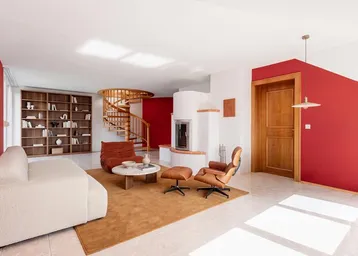 Geräumiges Wohnzimmer mit roter Akzentwand, Kamin und eleganter Wendeltreppe aus Holz.