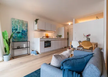 Heller offener Wohnbereich mit integrierter Küche, Essplatz und modernem Sofa auf Parkettboden.