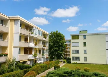 Mehrere Wohngebäude mit gepflegten Grünflächen und blauem Himmel an einem sonnigen Tag.