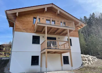 Modernes Holzhaus mit weißer Fassade und zwei Balkonen in alpiner Umgebung.
