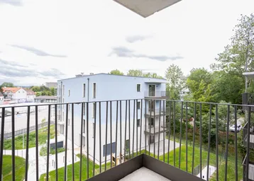 Blick vom Balkon auf ein modernes Wohngebäude und die umliegende grüne Landschaft.