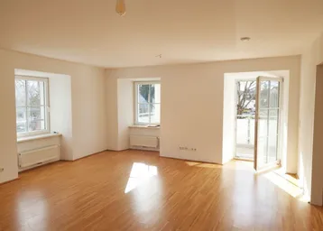 Helles Zimmer mit Parkettboden, weißen Wänden und Zugang zu einem Balkon.