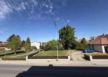Blick auf die ländliche Umgebung mit Straße, Grünflächen und angrenzenden Häusern unter blauem Himmel.