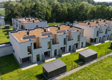 Moderne Reihenhäuser mit begrünten Flachdächern und Photovoltaikanlagen in ländlicher Umgebung.