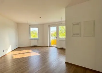 Heller, leerer Wohnbereich mit hochwertigem Parkettboden und Zugang zu einem sonnigen Balkon.