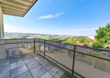 Geräumiger Balkon mit Fliesenboden und weitem Blick über die grüne Landschaft und umliegende Häuser.