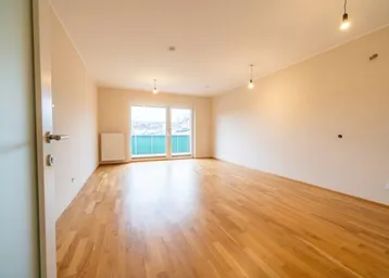 Heller, leerer Raum mit schönem Holzboden, großen Fenstern und direktem Zugang zu einem Balkon.