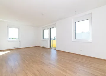 Helles, leeres Zimmer mit Laminatboden, weißen Wänden und Zugang zu einem Balkon.