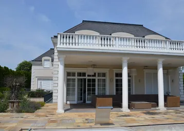 Elegante Villa mit klassischer Architektur, großer Terrasse, Säulen und Balkon.
