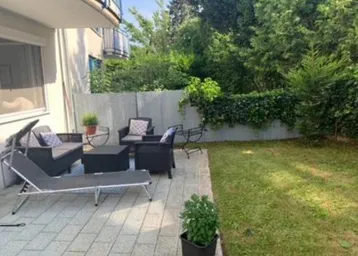 Gepflasterte Terrasse mit Gartenmöbeln und angrenzender Rasenfläche, umgeben von Hecken.