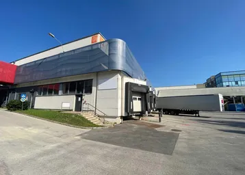 Außenansicht eines Industriegebäudes mit Laderampen und einem geparkten LKW-Anhänger unter blauem Himmel.