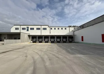 Außenansicht eines modernen Logistikgebäudes mit mehreren Laderampen und großem Vorplatz für Lieferfahrzeuge.