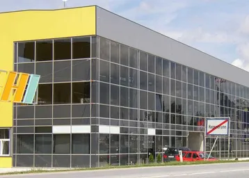 Modernes Gewerbegebäude mit auffälliger gelber Fassade und großer Glasfront, gut sichtbar von der Straße.
