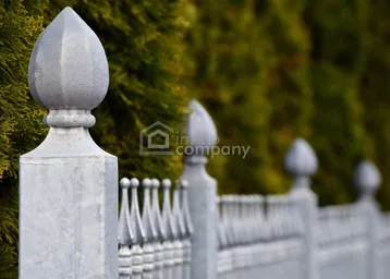 Dekorativer Metallzaun mit spitzen Ornamenten vor einer grünen Hecke, der das Grundstück abgrenzt.