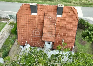 Draufsicht auf das Haus mit Ziegeldach und zwei Schornsteinen, umgeben von Grünflächen.