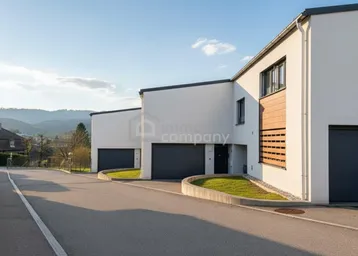 Moderne Reihenhäuser mit weißen Fassaden, dunklen Garagentoren und gepflegter Auffahrt an einem sonnigen Tag.