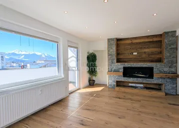 Helles Wohnzimmer mit Holzboden, modernem Kamin und beeindruckendem Bergblick durch große Fenster.