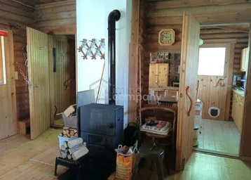 Rustikaler Wohnbereich mit einem Holzofen und Holzböden, umgeben von Blockwänden.