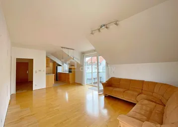 Offener Wohnbereich im Dachgeschoss mit Holzboden, Sofa und Blick auf die angrenzende Küche.