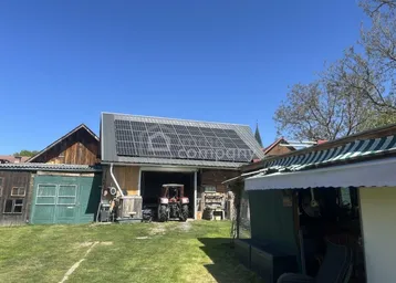 Scheunengebäude mit Photovoltaikanlage auf dem Dach und einem Traktor davor.