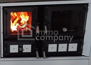 Traditioneller Holzofen mit integriertem Backfach und sichtbarem Feuer in einer Küche.