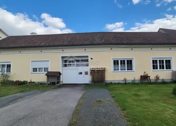 Einfamilienhaus mit heller Fassade, braunem Ziegeldach, mehreren Fenstern mit Rollläden und großer Garagentür.