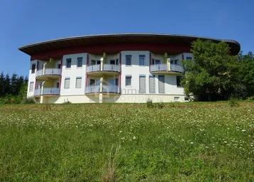 Modernes Gebäude mit runder Architektur, vielen Balkonen und umgeben von grüner Natur.