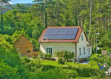 Landhaus mit Photovoltaikanlage auf dem Dach, umgeben von üppiger grüner Natur und Wald.