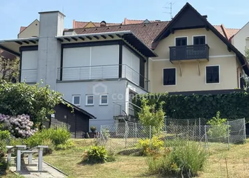 Ansicht des Hauses mit Gartenbereich und angrenzendem Nebengebäude unter blauem Himmel.