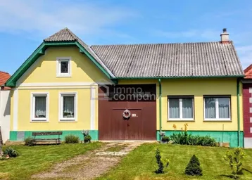 Traditionelles Landhaus mit gelber Fassade, grünem Dachgiebel und großem Holztor.